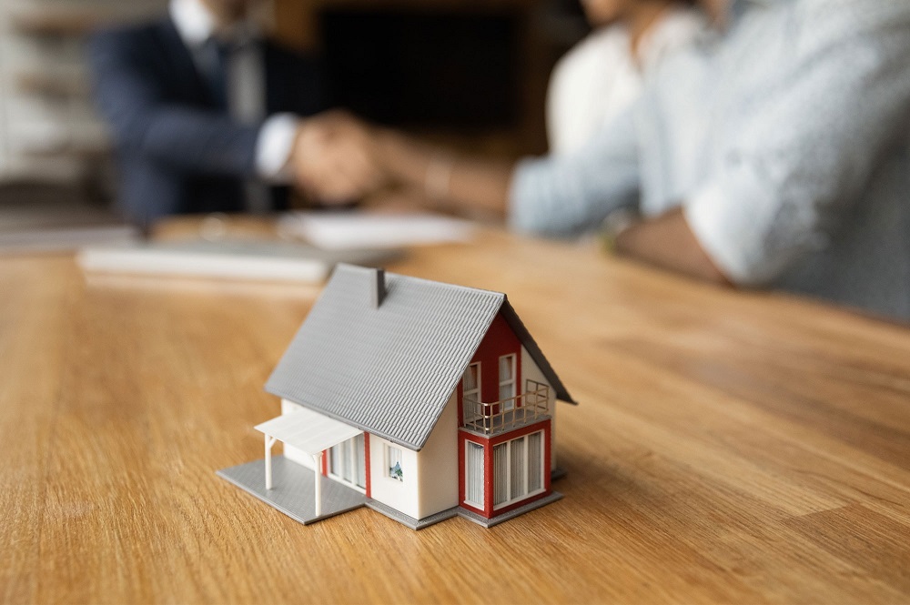 Model house on table while buyers sign paperwork for purchasing investment property through a trust in Australia.